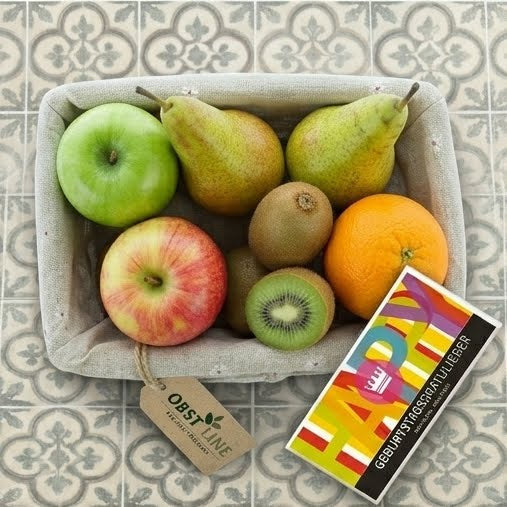 Obstkorb Happy Fruit-Day, Draufsicht auf Äpfel, Birnen, Kiwis, Orange und Geburtstagsschokolade